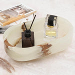 White onyx oval marble trinket dish holding a reed diffuser and perfume beside books