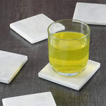 White square coasters under a glass of yellow wine on a dark wood table