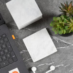 White square marble coasters on a dark desk beside a laptop and succulent