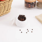 White marble salt cellar filled with black peppercorns, lid resting beside it, 3 inches wide and tall