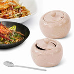 Two 4 inch verona marble salt cellars with lids and a stainless steel spoon beside plated noodle dishes