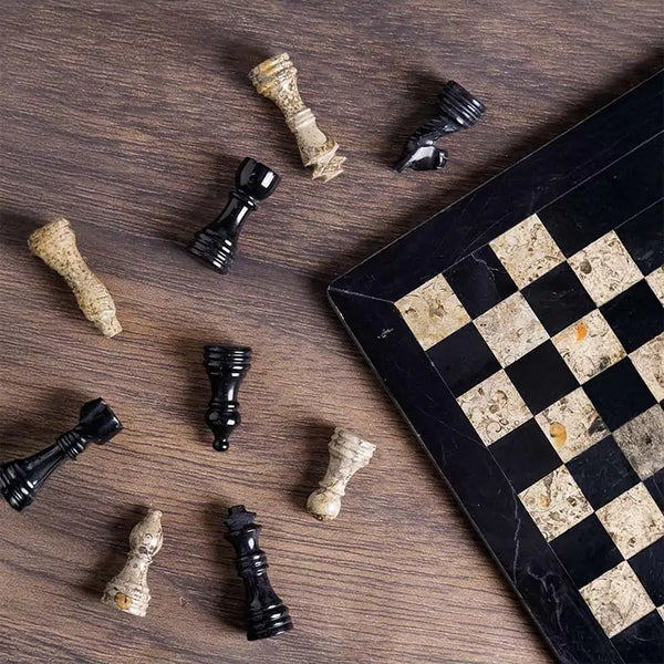 Black and fossil coral marble chess set 12 inch — pieces scattered on dark wood surface showing black marble and fossil coral stone detail by RADICALn
