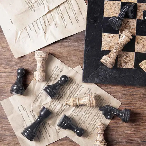 black and fossil coral marble chess pieces scattered on book pages — board corner detail by RADICALn