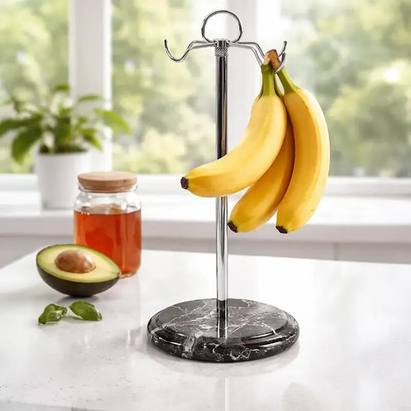 Black marble banana holder on a kitchen counter holding a bunch of bananas, with avocado and honey nearby