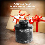 Black marble butter keeper presented as a gift in front of a wrapped box with a red ribbon