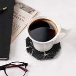 Black octagon marble coaster under a white coffee cup beside a newspaper and glasses