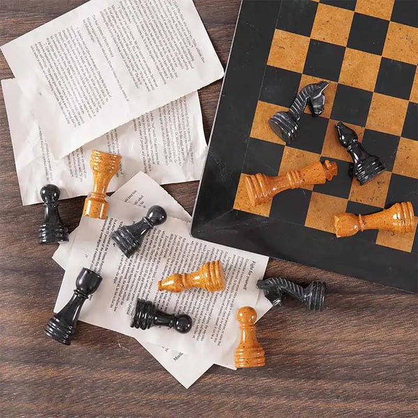 Black marble and golden marble chess pieces scattered on book pages — board corner detail by RADICALn