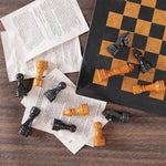 Black marble and golden marble chess pieces scattered on book pages — board corner detail by RADICALn