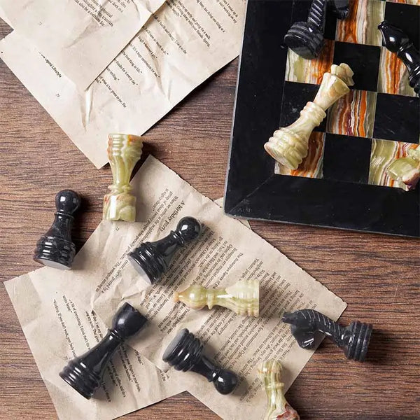 Black marble and multi green onyx chess pieces scattered on book pages — board corner detail by RADICALn