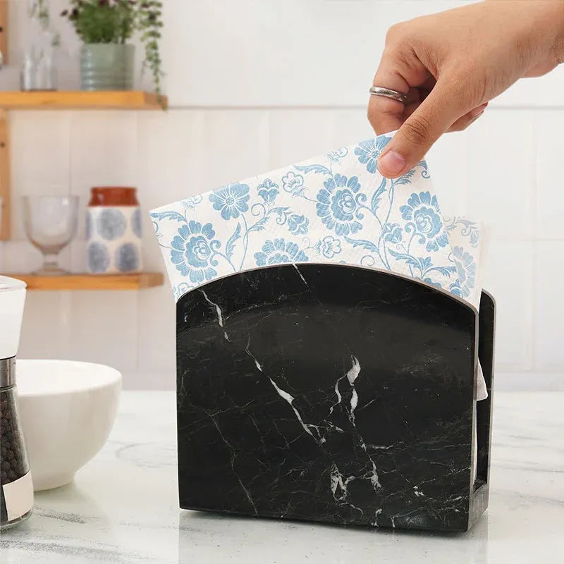Hand pulling a floral napkin from a black marble napkin holder in a kitchen