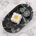 Black marble oval tray holding a candle, earrings and a pinecone on marble