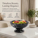 Black marble pedestal fruit bowl holding fruit on a dining table, noting its natural stone and polished finish