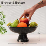 Black marble pedestal fruit bowl measuring 10 inches wide and 5 inches tall, filled with fruit as a hand reaches in