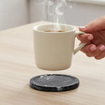 Round black marble coaster on a wooden table as a hand lifts a cup of coffee