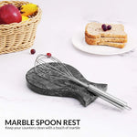 Black marble spoon rest holding a whisk on a kitchen counter with fruit and toast