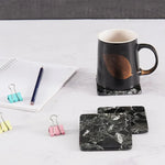 Square black marble coasters beside a black mug and notepad on a desk