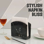 Black marble table napkin holder with folded napkins beside a wine glass and gold fork
