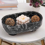 Black footed marble trinket bowl holding a candle and rattan balls on a coffee table