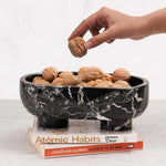 Black marble trinket bowl on books, filled with walnuts, hand reaching in