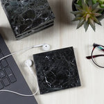 Stacked black square marble coasters on a wooden desk with a laptop and glasses