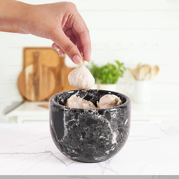 Hand placing a garlic bulb into an open black zebra marble garlic keeper filled with garlic