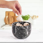 Hand placing a garlic bulb into an open black zebra marble garlic keeper filled with garlic