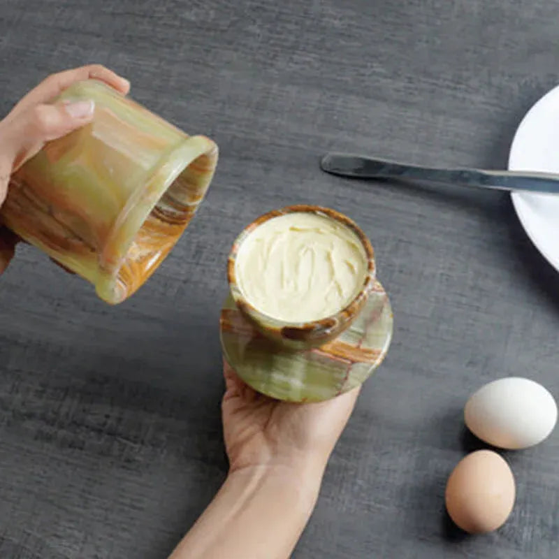 Hands lifting the crock base off a green onyx marble butter keeper to reveal butter packed in the lid