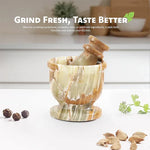Green onyx marble mortar and pestle on a kitchen counter with whole peppercorns, cardamom pods and fresh coriander