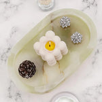 Green onyx marble oval tray holding a candle, earrings and a pinecone on marble