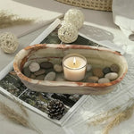 Green onyx oval marble tray holding a candle and river pebbles on a styled coffee table
