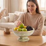 Woman placing a green apple into a green onyx marble pedestal fruit bowl full of fruit on a coffee table