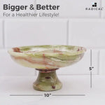 Green onyx marble pedestal fruit bowl measuring 10 inches wide and 5 inches tall, filled with fruit as a hand reaches in