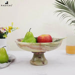 Green onyx marble pedestal fruit bowl raised on a footed stem holding a pear and apple, styled with flowers and juice