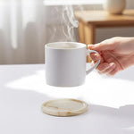Round green onyx marble coaster on a wooden table as a hand lifts a cup of coffee