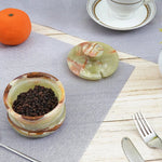 Green onyx marble salt cellar filled with peppercorns, notched lid set aside on a table with fruit and cutlery