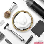 Green onyx marble shaving bowl with lather flanked by razors, brush and towel on floor
