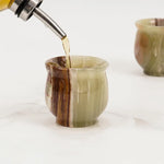 Drink being poured into a green onyx marble shot glass on a marble surface