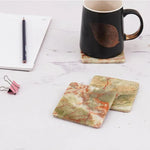 Square green onyx marble coasters beside a black mug and notepad on a desk