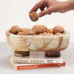Green onyx marble trinket bowl on books, filled with walnuts, hand reaching in