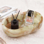 Green onyx oval marble trinket dish holding a reed diffuser and perfume beside books