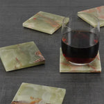 Green onyx square coasters under a glass of red wine on a dark wood table