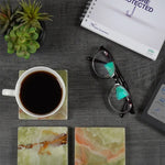 Green onyx square marble coasters on a desk with a printed mug, notebook and glasses