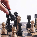 Hand lifting black marble bishop piece — black and fossil coral chess pieces in starting position by RADICALn