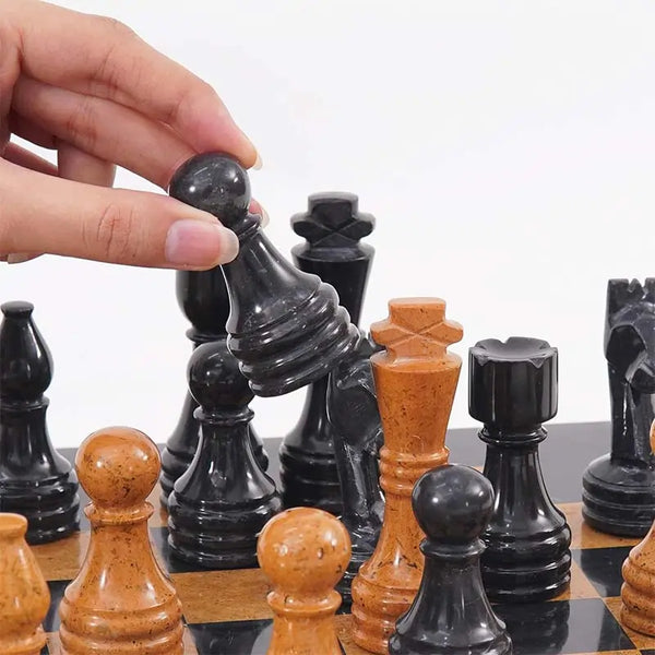 Hand lifting black marble bishop piece — Black marble and golden marble chess pieces in starting position by RADICALn