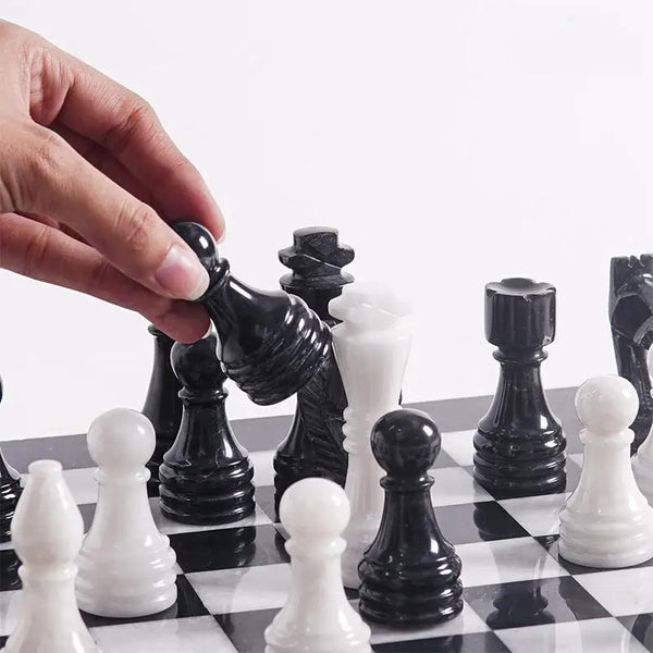 Hand lifting black marble bishop piece — black and white chess pieces in starting position by RADICALn
