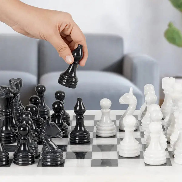 Hand lifting black marble pawn piece — white and black marble chess set 15 inch with storage box in home living room setting by RADICALn