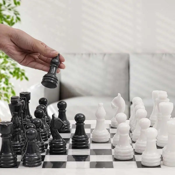 Hand lifting black marble rook piece — white and black marble chess set 15 inch standard set in bright minimalist home setting by RADICALn