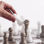 Hand lifting white marble bishop piece — Oceanic grey and white marble chess pieces in starting position by RADICALn