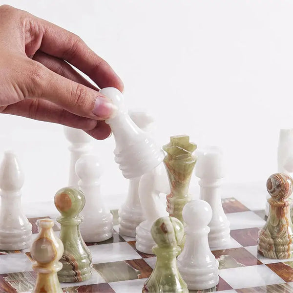 Hand lifting white marble bishop piece — white and green onyx chess pieces in starting position by RADICALn