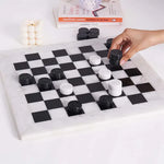 Hand placing black marble checkers disc mid-game — white and black marble checkers set 15 inch with books and candle by RADICALn